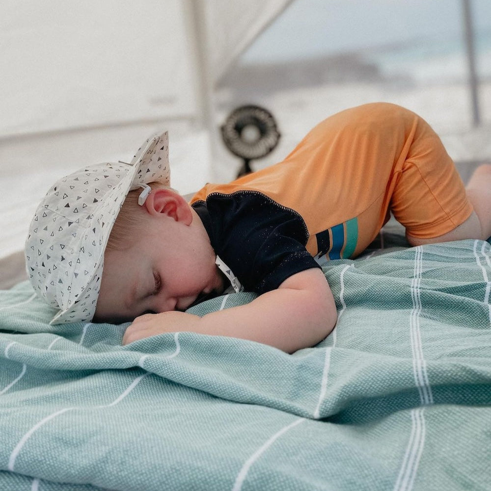 A baby is sleeping face down on a teal Wetcat Turkish towel